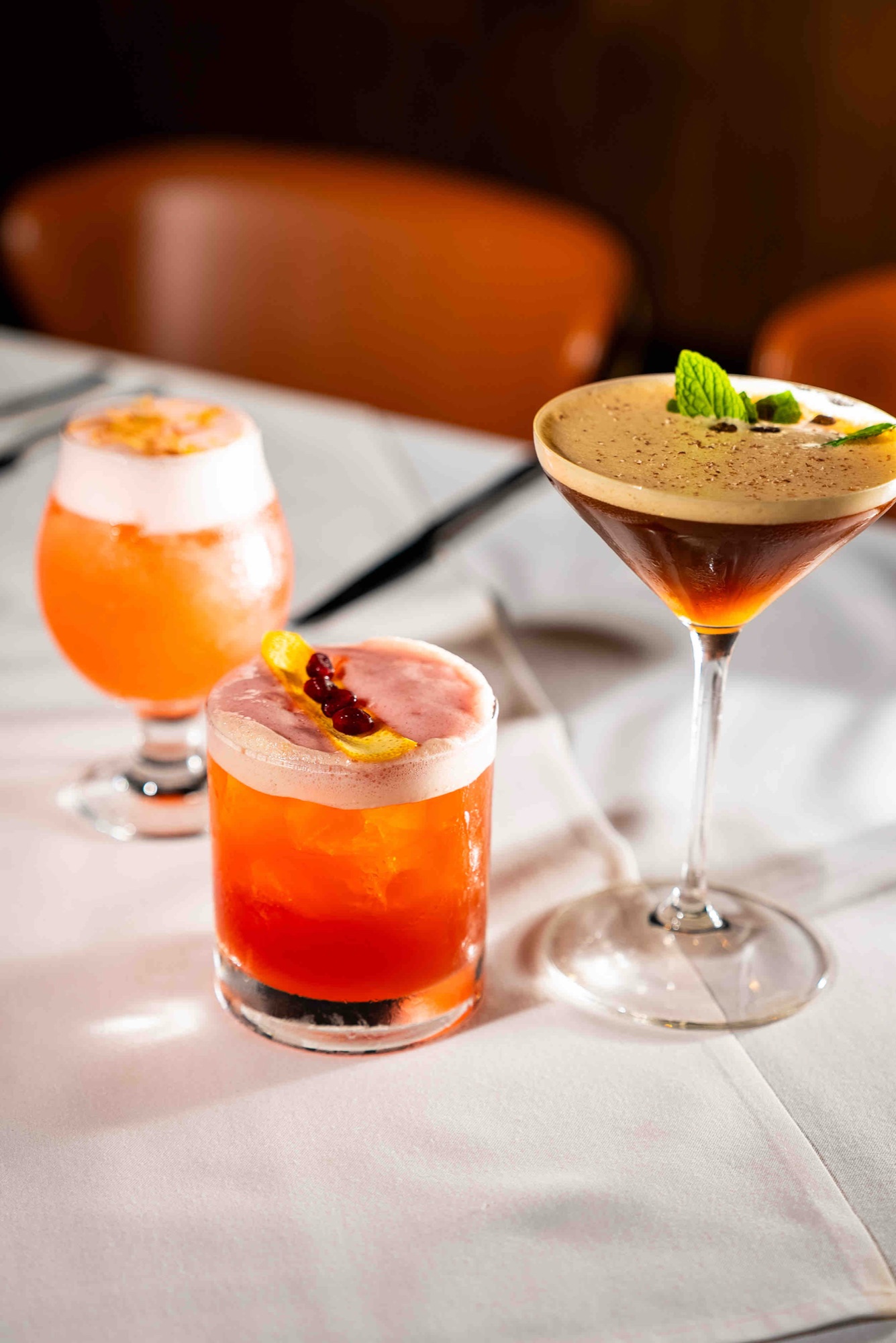 A trio of craft cocktails — an espresso martini, a coupe and a rocks cocktail — on a candlelit table at The Arthur J