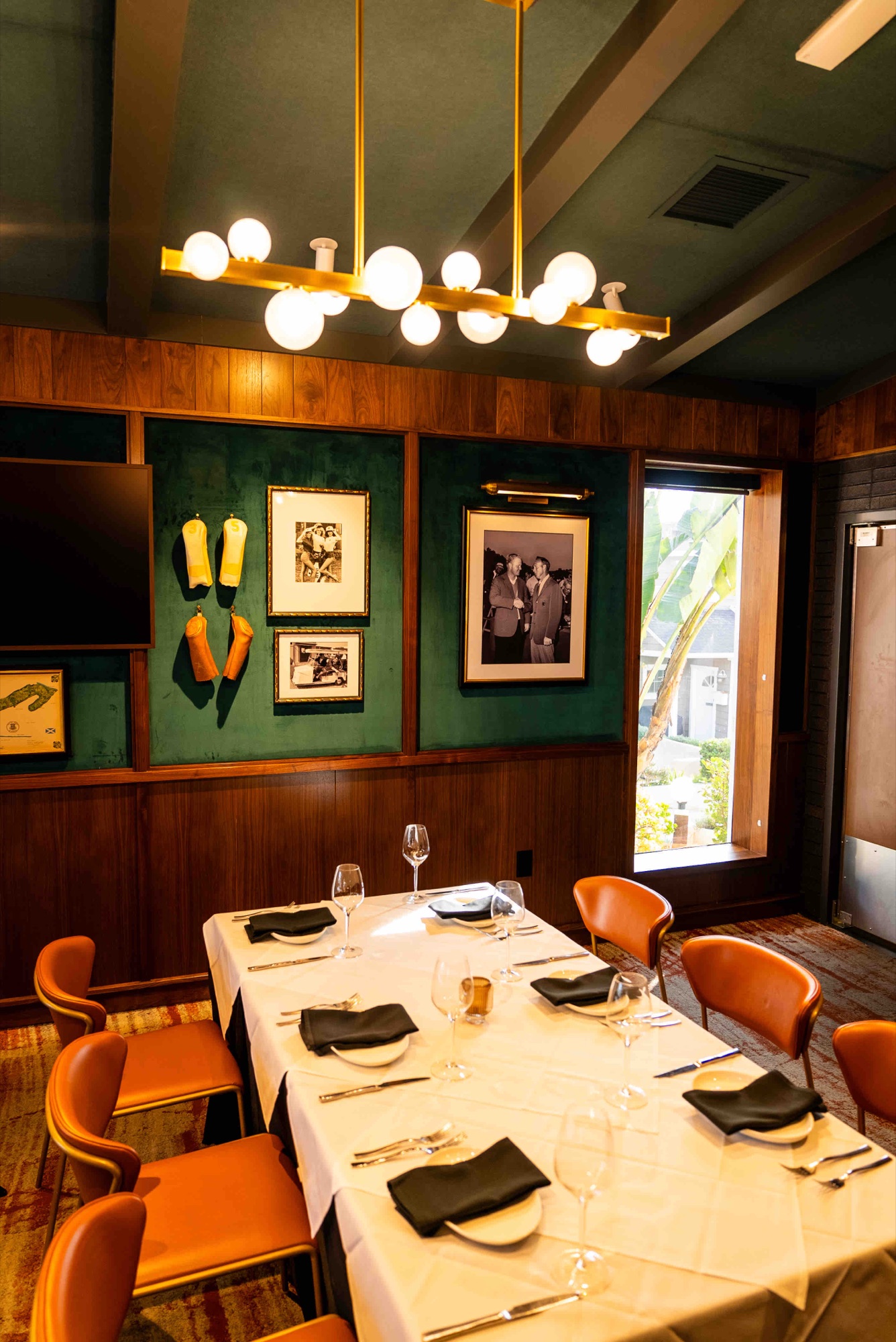Private dining room with a long set table, brass globe chandelier and emerald green walls