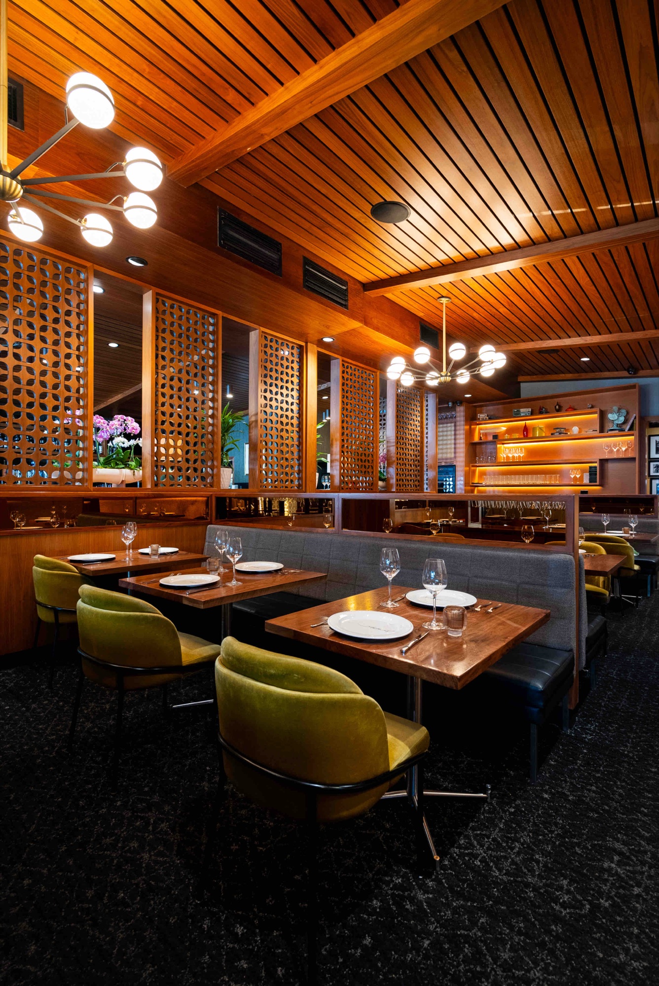 Emerald green velvet banquette booths beneath warm brass lighting and framed black-and-white portraits in the dining room at The Arthur J