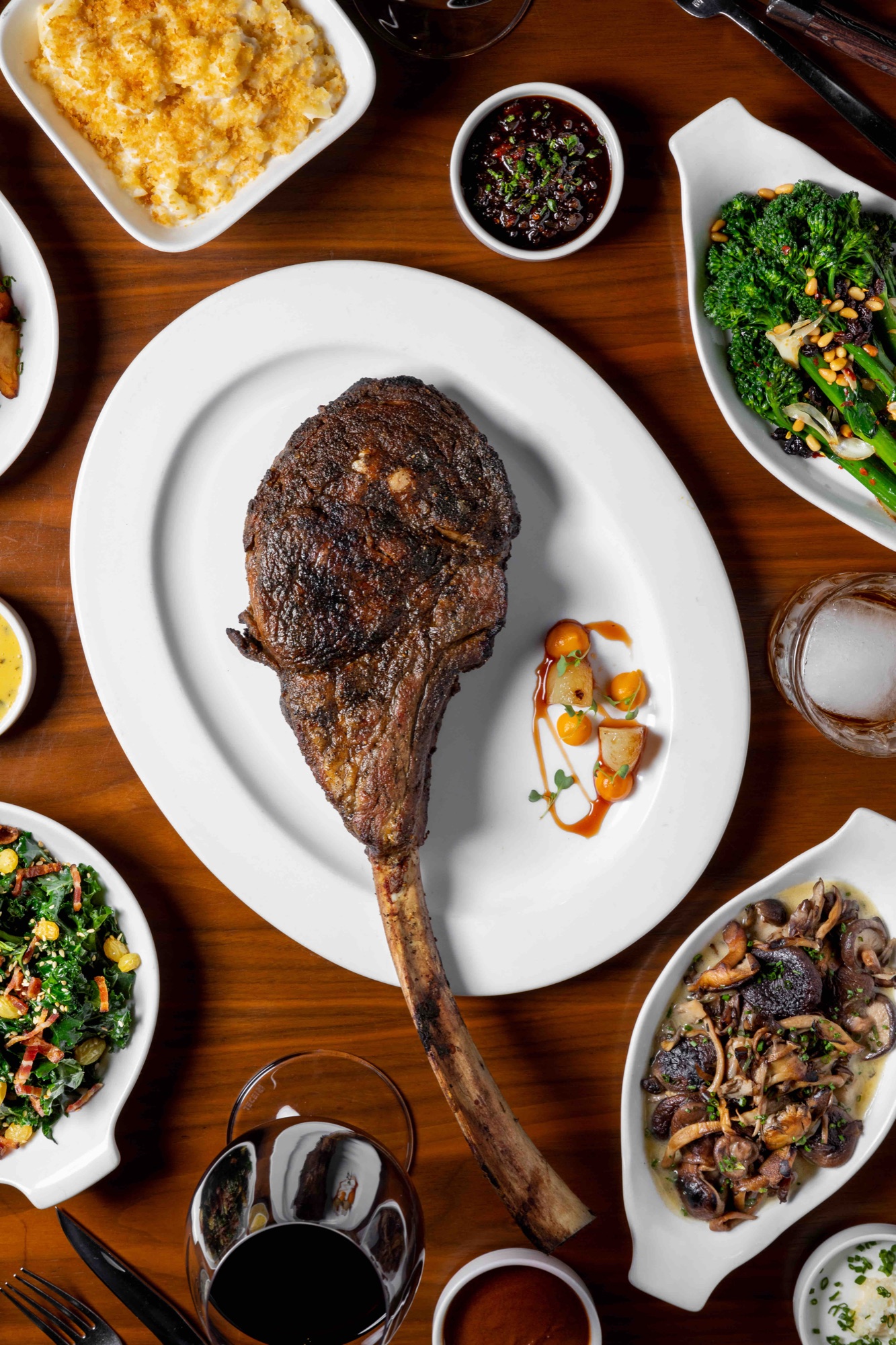 An overhead grilled bone-in tomahawk steak surrounded by side dishes at The Arthur J